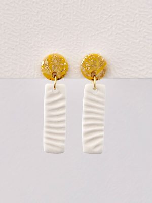 Pendientes colgantes color arena con partículas doradas y base rectangular blanca con relieve de concha